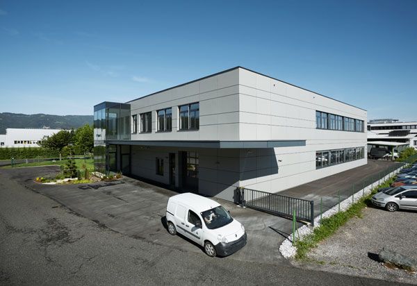 Ein modernes Firmengebäude mit einem Parkplatz und einem Lieferwagen davor.